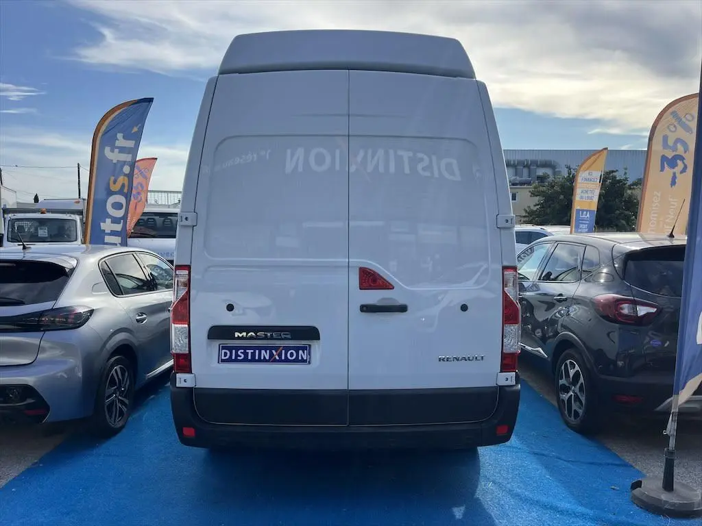 Vue arrière d'un utilitaire Renault Master blanc garé entre deux voitures, avec logo Distinxion visible sur la porte.