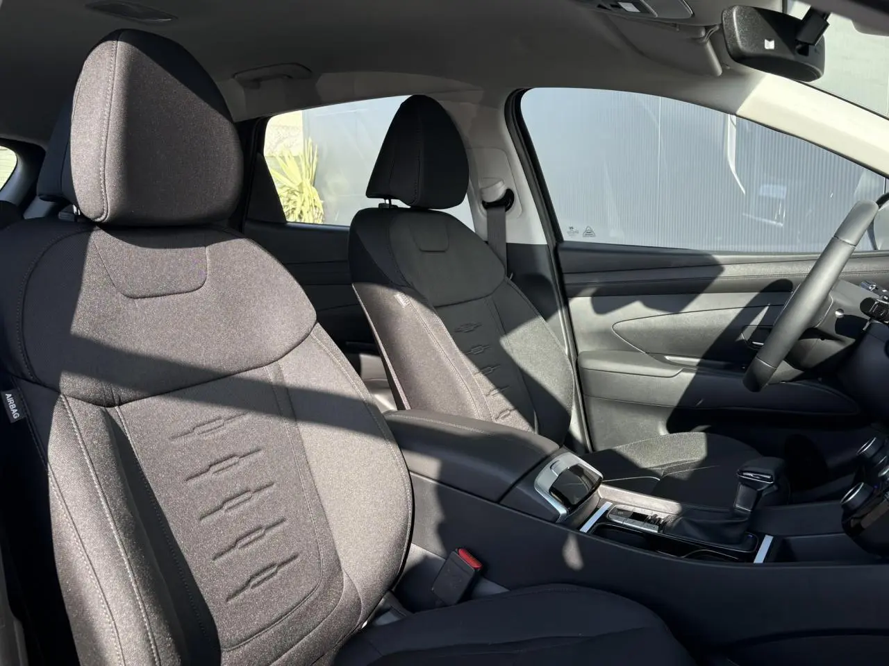 Vue intérieure côté conducteur du Hyundai Tucson 2025 avec sièges tissu noirs et console centrale moderne.