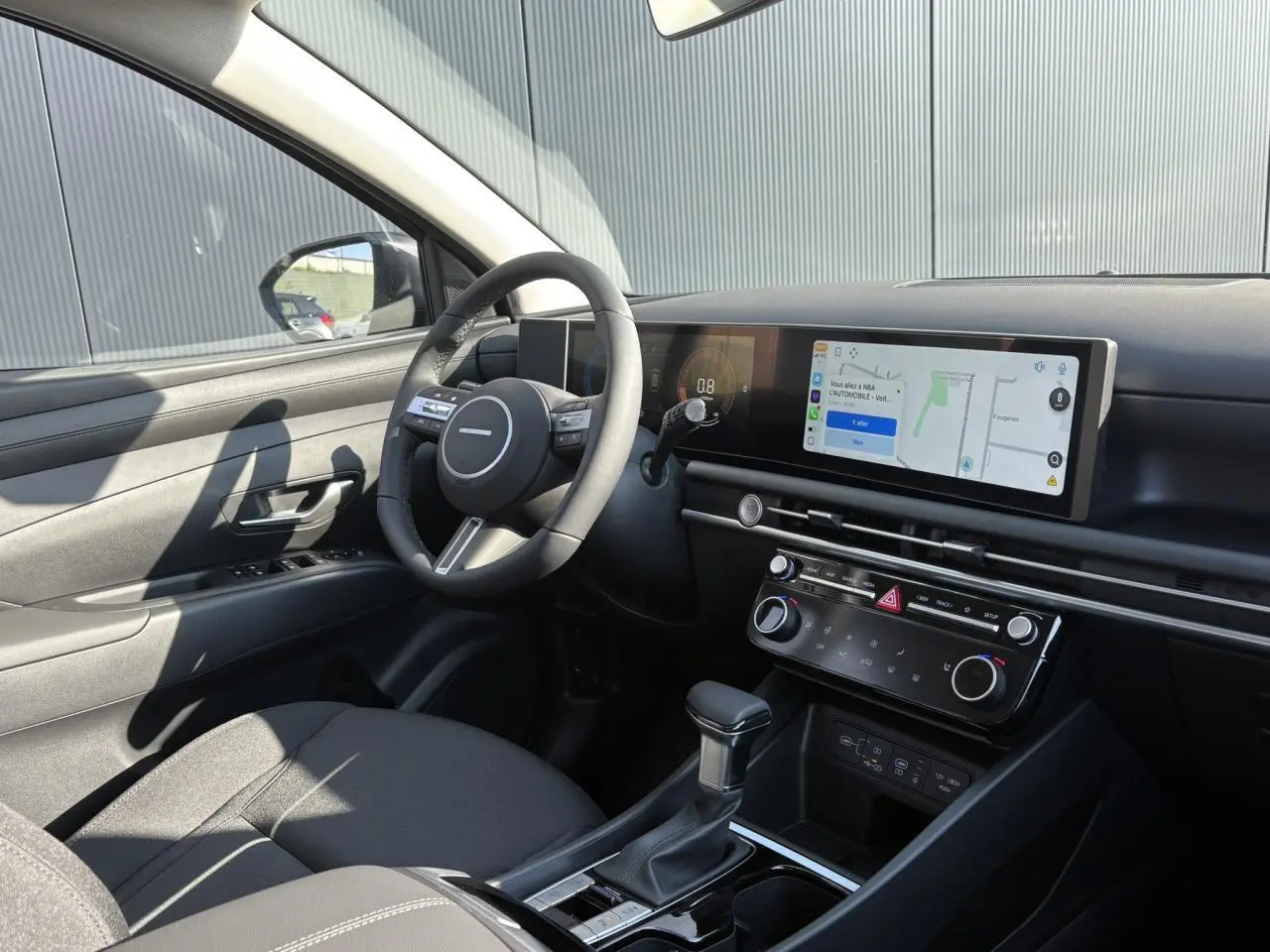 Intérieur avant gauche du Hyundai Tucson 2025 noir, tableau de bord moderne avec écran tactile panoramique et volant cuir.