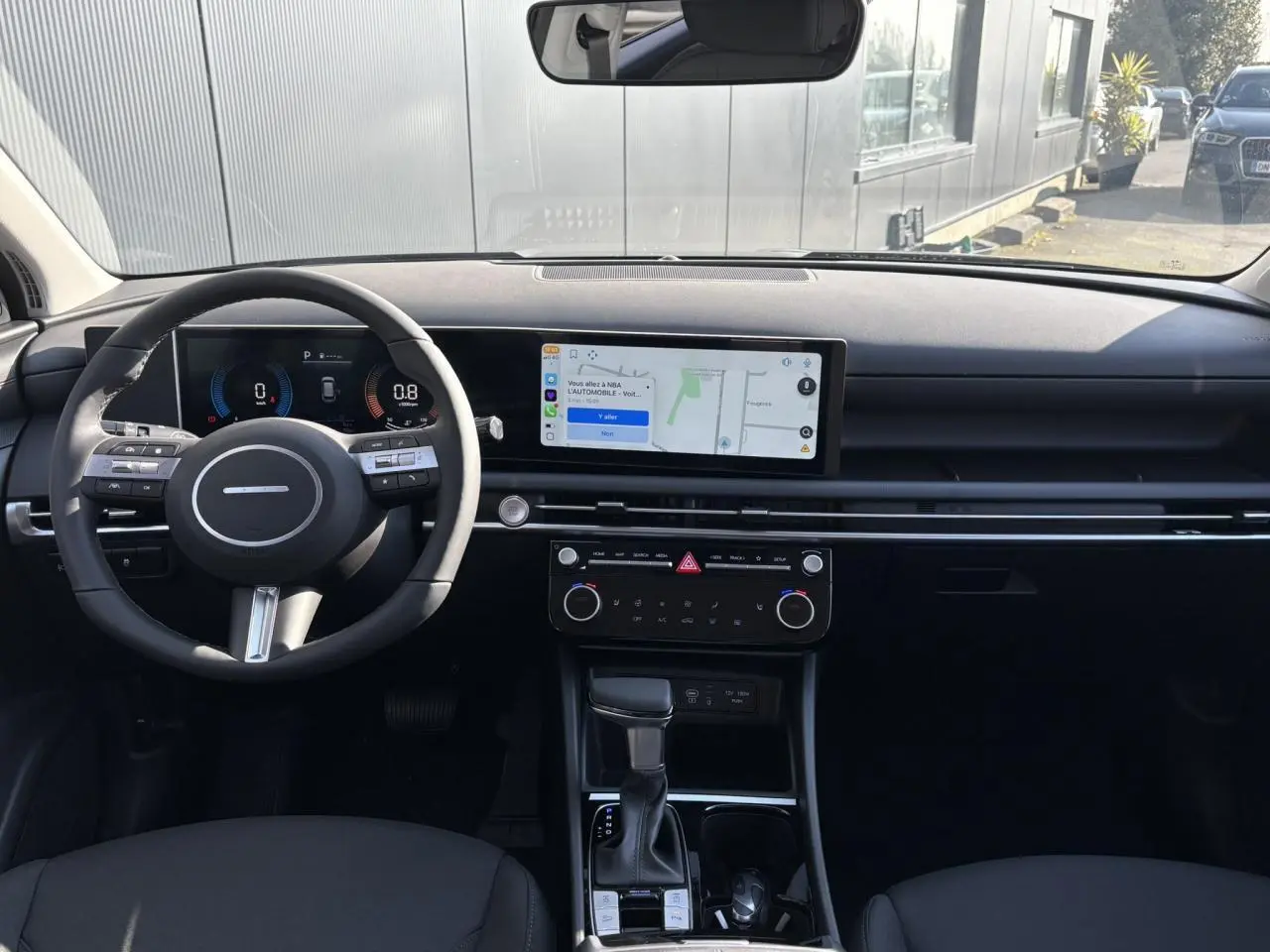 Vue intérieure frontale du tableau de bord du Hyundai Tucson 2025 avec écran tactile large et volant multifonction noir.