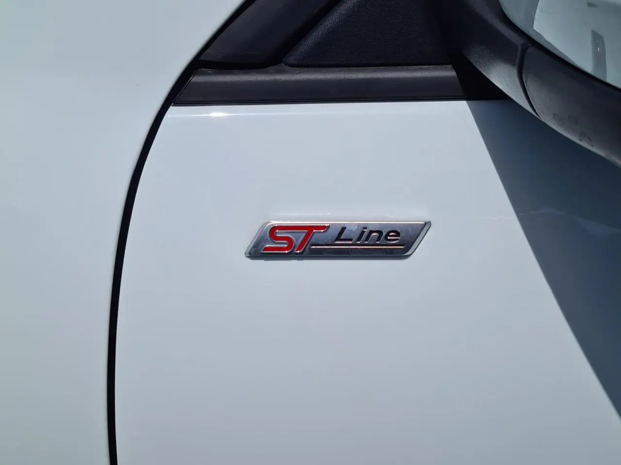 Gros plan sur l'écusson ST-Line rouge et noir sur la porte blanche glacier d'un Ford Kuga hybride rechargeable.