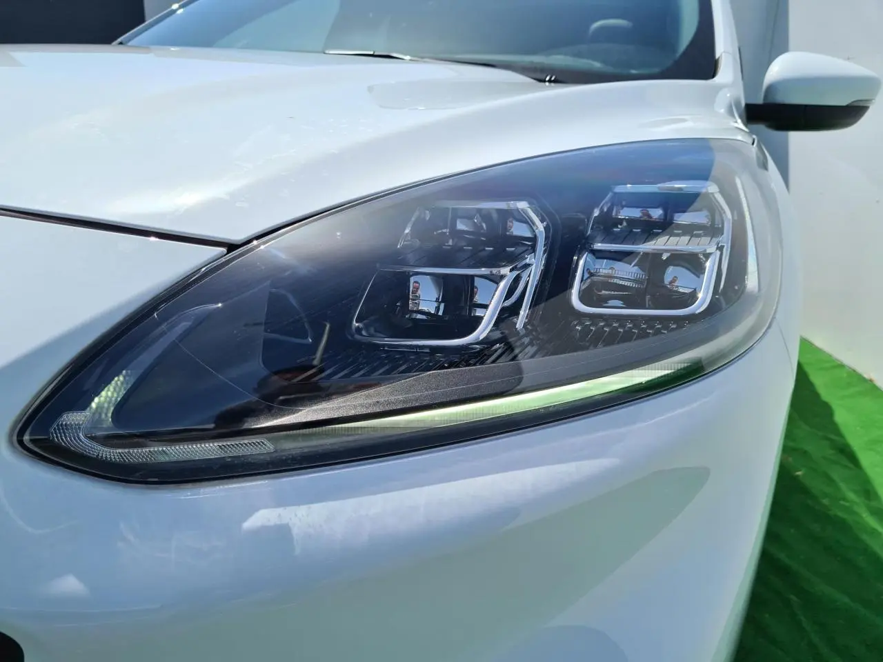 Gros plan sur le phare avant droit du Ford Kuga blanc glacier, mettant en valeur son design LED moderne.