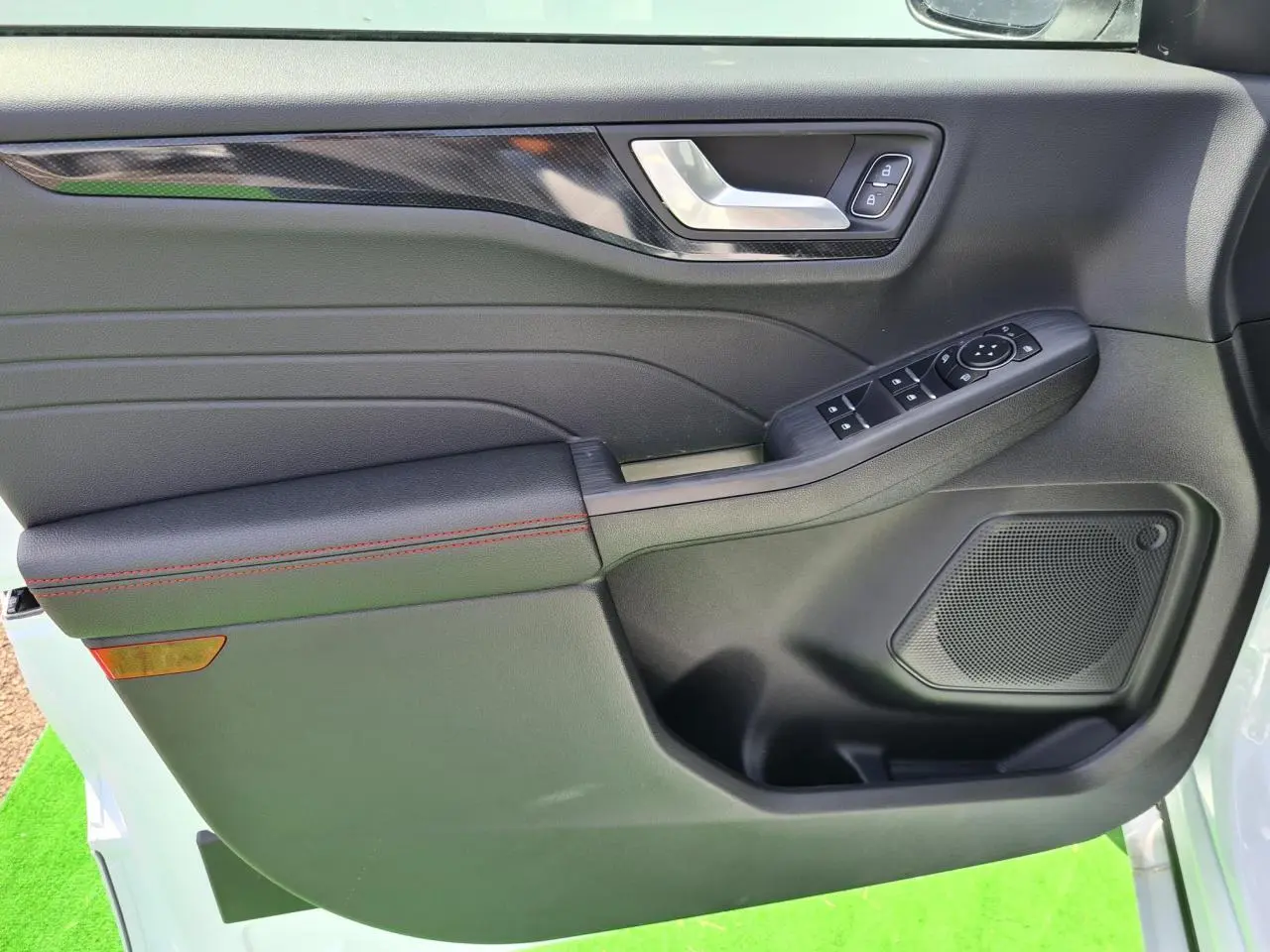 Gros plan sur la porte avant gauche du Ford Kuga blanc glacier, avec surpiqûres rouges et commandes électriques.