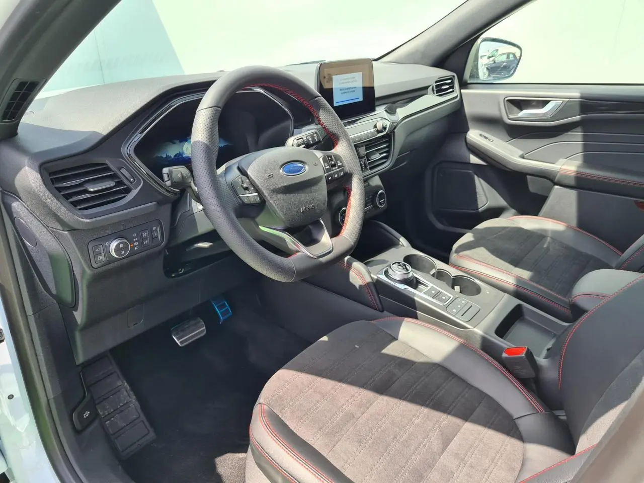 Intérieur avant droit du Ford Kuga blanc Glacier 2022, sièges sport noirs avec surpiqûres rouges et volant ST-Line.