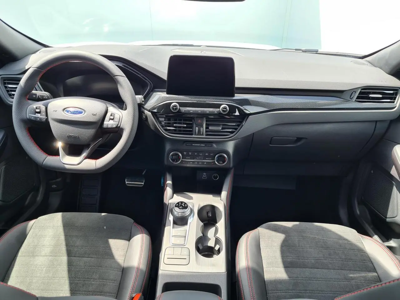 Intérieur avant du Ford Kuga blanc glacier 2022, tableau de bord moderne avec écran tactile et volant sport à surpiqûres rouges.