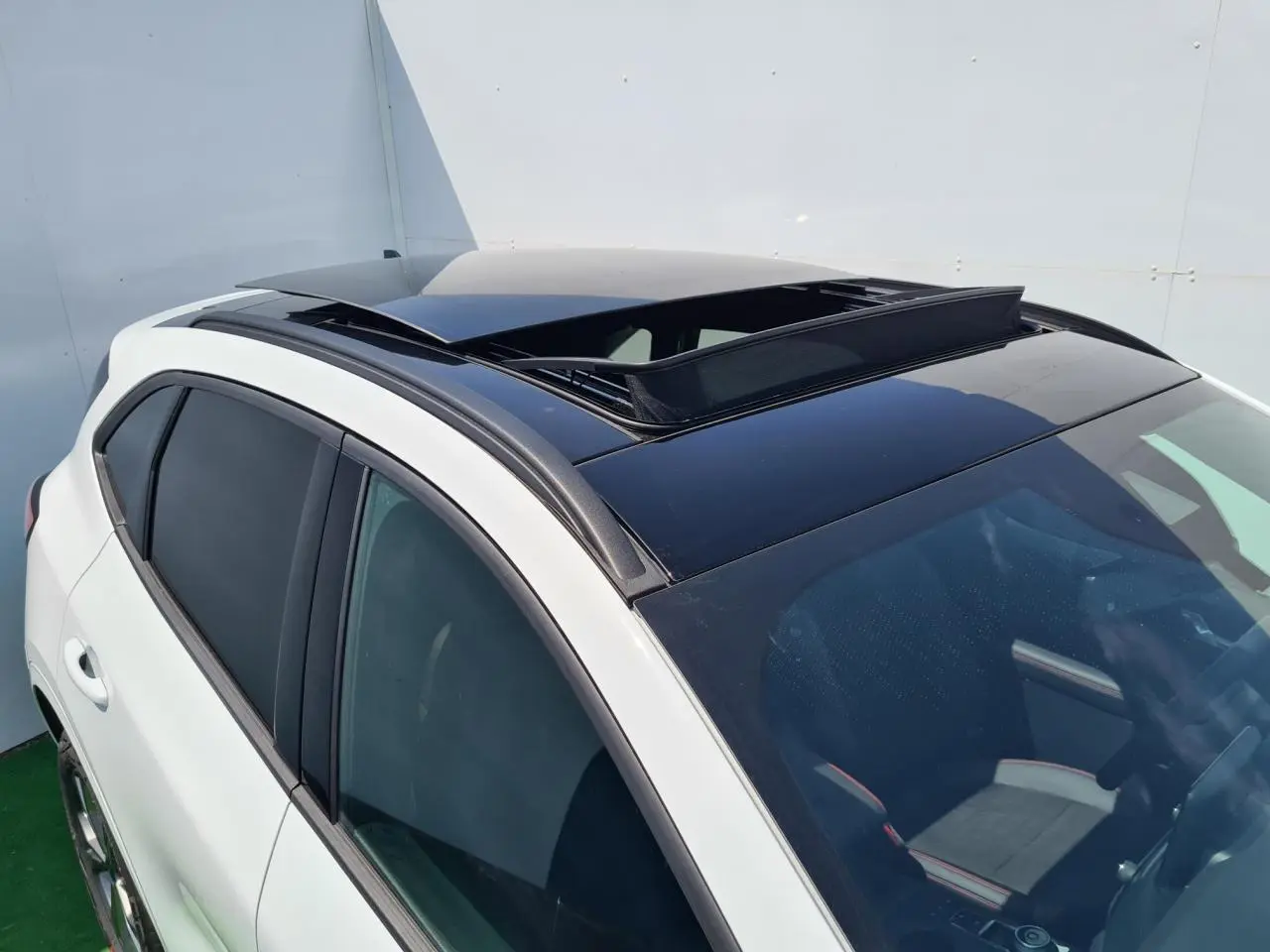 Vue 3/4 avant droit du Ford Kuga blanc glacier avec toit ouvrant panoramique ouvert et vitres surteintées.