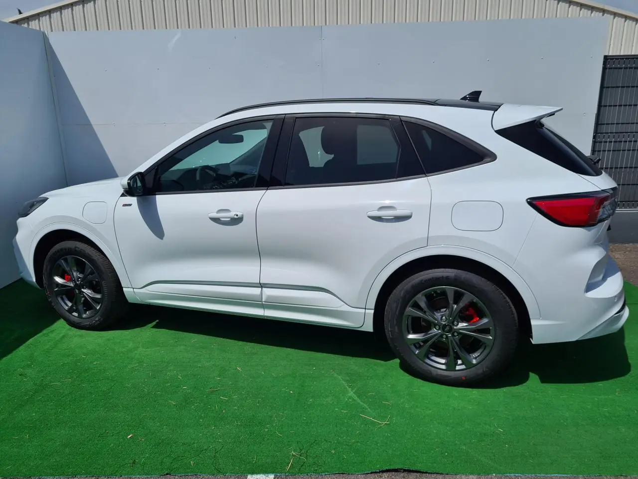 Profil côté gauche du Ford Kuga blanc glacier 2022 avec jantes alliage noires et étriers rouges visibles.