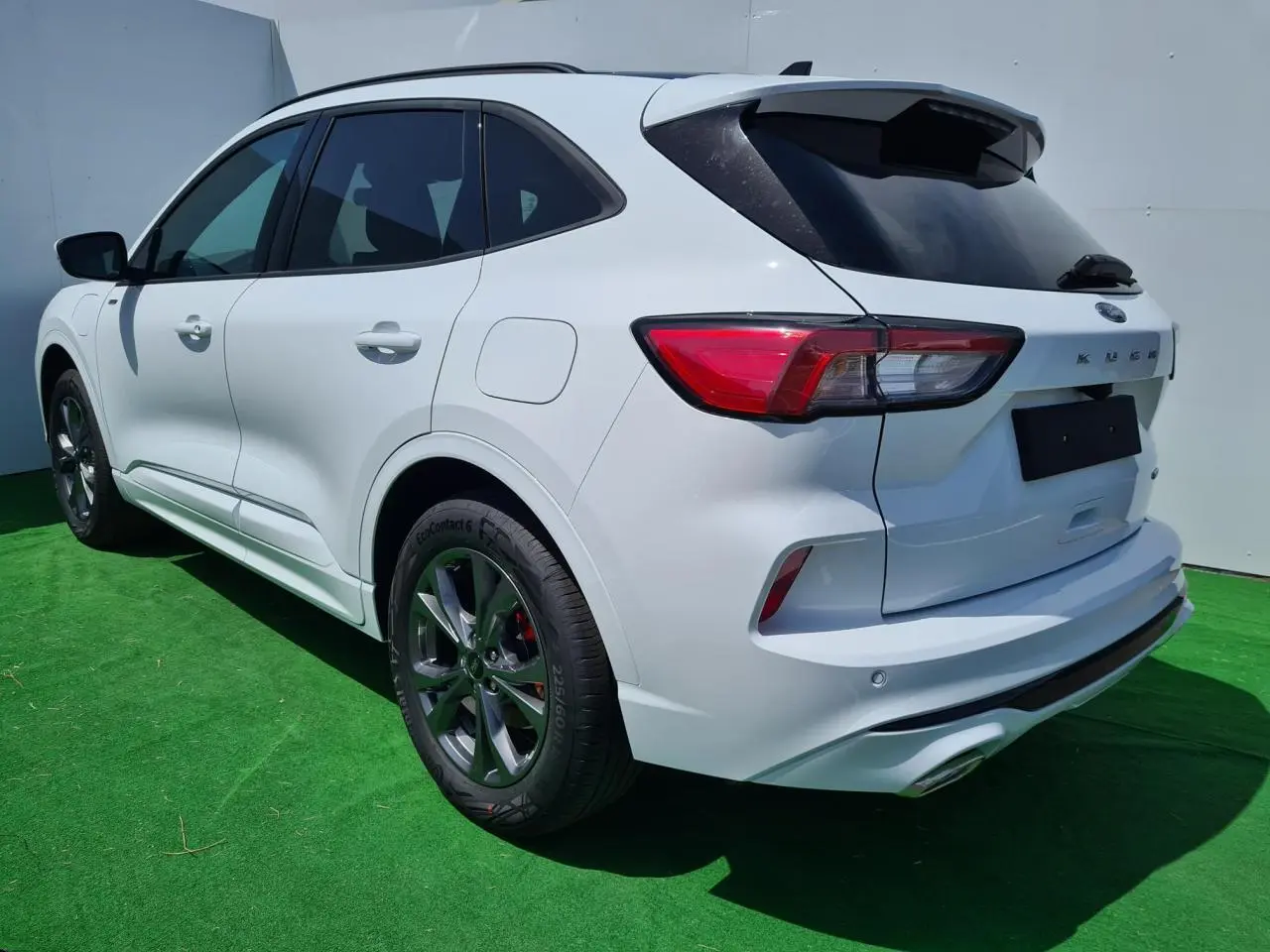 Ford Kuga blanc glacier en 3/4 arrière droit, avec jantes alliage 18 pouces et barres de toit noires visibles.