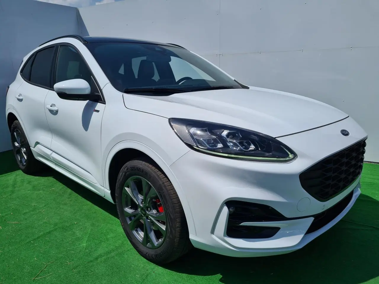 Ford Kuga blanc glacier en 3/4 avant droit avec jantes alliage et calandre noire ST-Line visible.