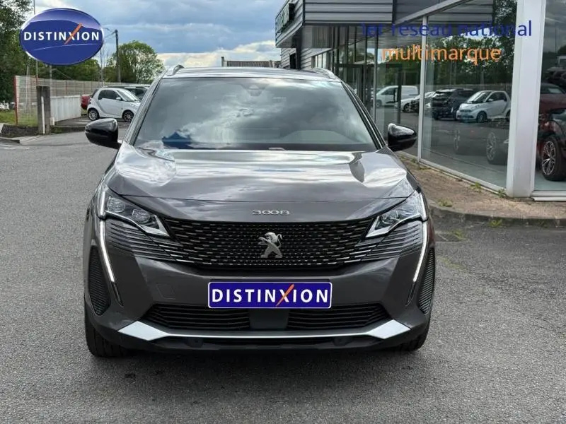 Vue avant d'un Peugeot 3008 gris Platinium avec calandre noire et feux LED allumés, stationné devant un bâtiment vitré.