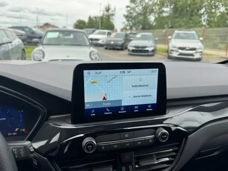 Vue intérieure du tableau de bord du Ford Kuga 2023 avec écran tactile de navigation allumé et commandes audio visibles.