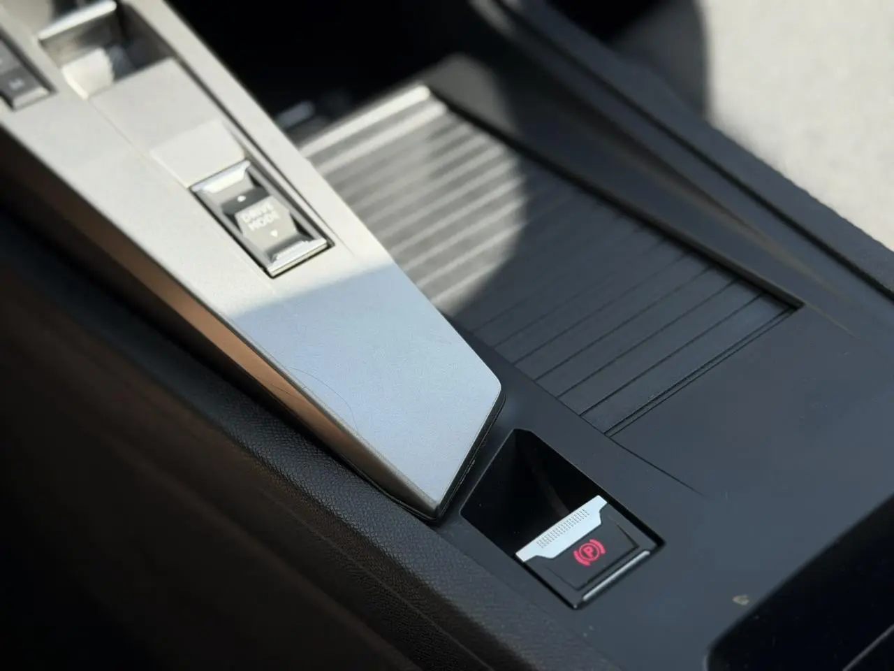 Gros plan sur la console centrale intérieure de la Peugeot 308 gris Artense, avec frein de parking électrique et bouton Drive Mode.