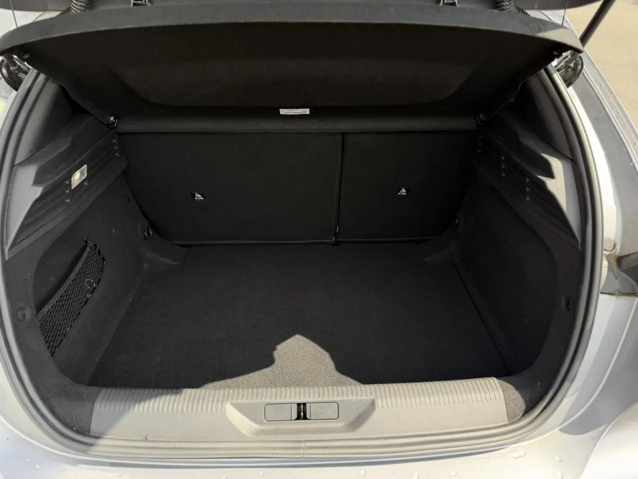 Vue intérieure du coffre ouvert d'une Peugeot 308 gris Artense, montrant l'espace de rangement vide et les finitions en tissu noir.
