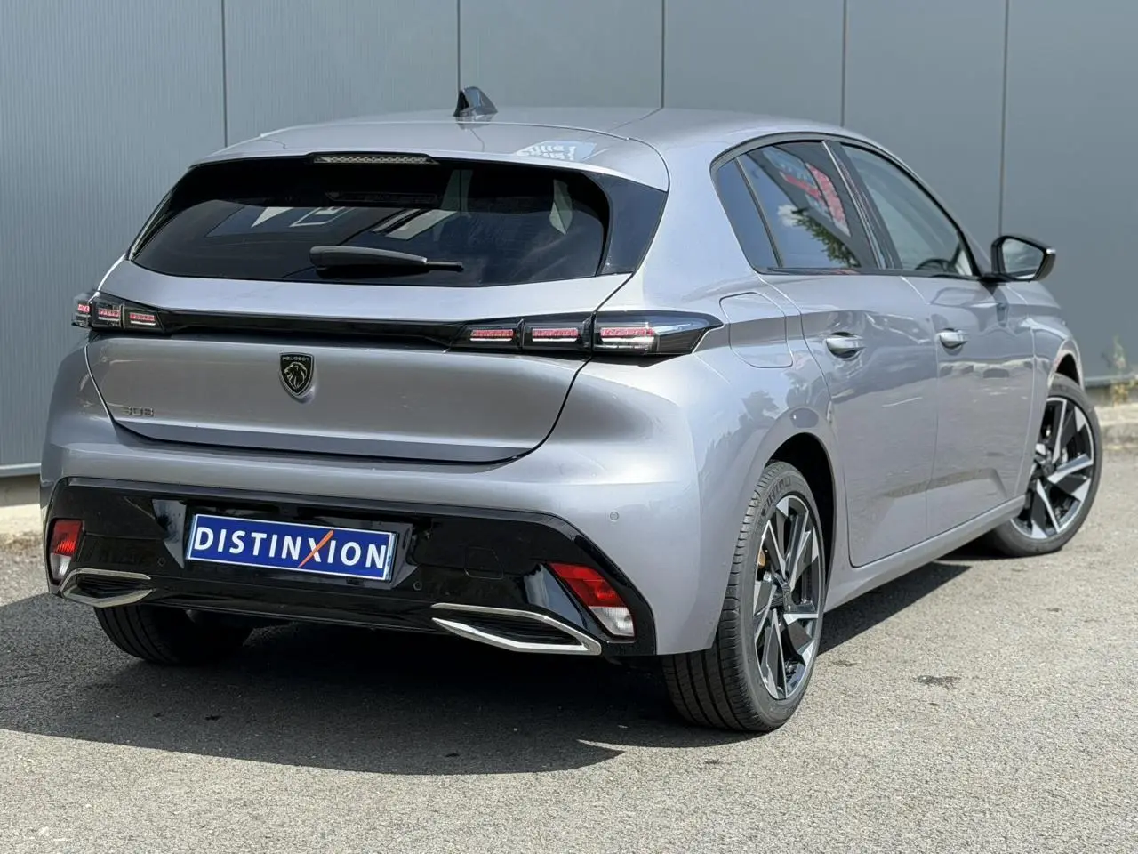 Vue 3/4 arrière droite d'une Peugeot 308 gris Artense avec jantes alliage et bandeau noir brillant entre feux arrière.