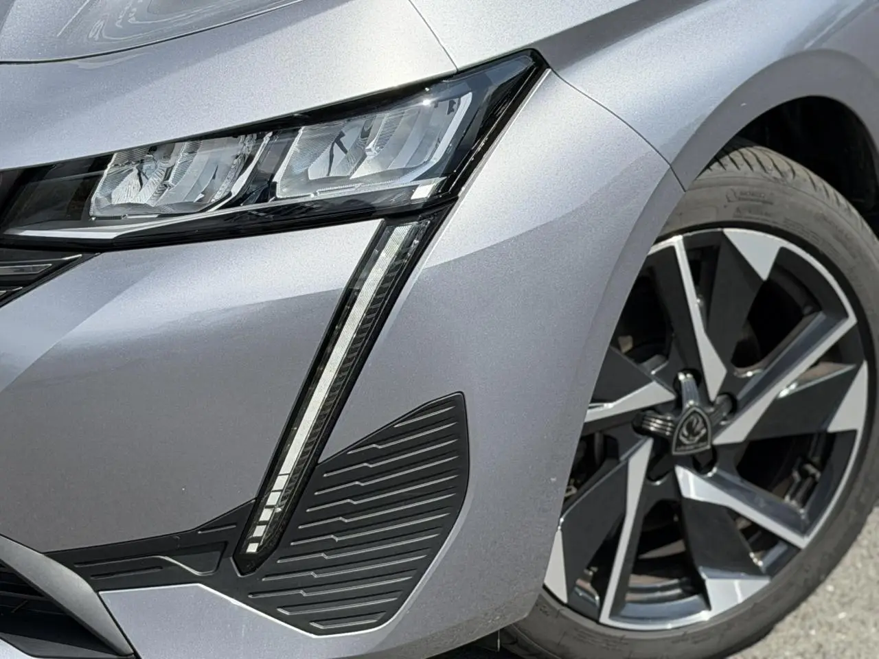 Gros plan sur le phare avant droit et la jante alliage 17'' gris Artense métallisée du Peugeot 308 2025.