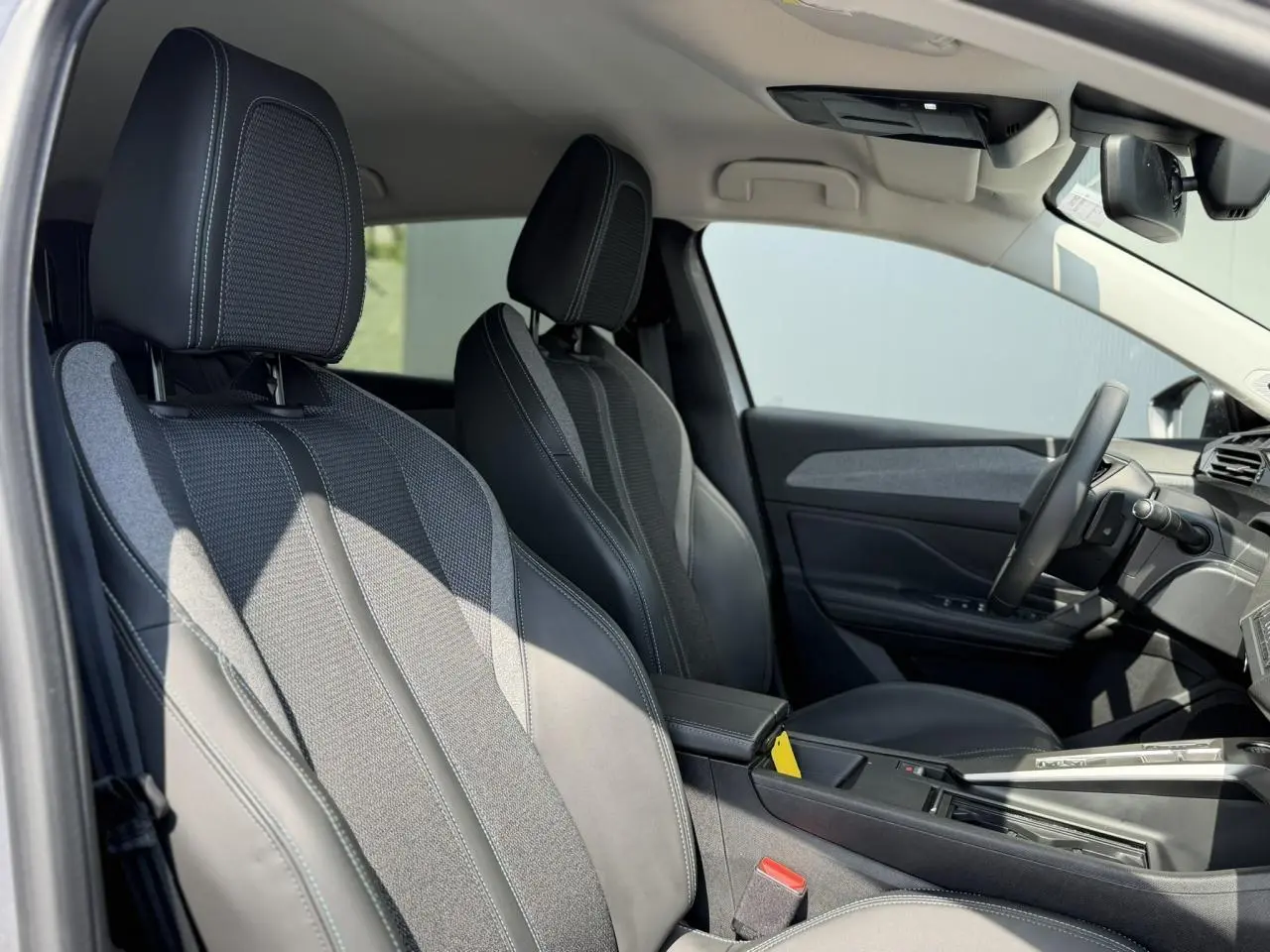 Vue intérieure côté conducteur de la Peugeot 308 2025 avec sièges en cuir et tissu gris, volant cuir et accoudoir central.