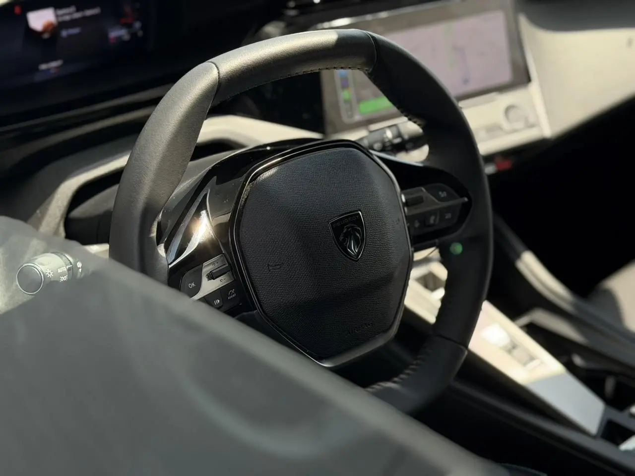 Gros plan sur le volant cuir noir du Peugeot 308 2025 avec tableau de bord numérique et écran tactile en arrière-plan.