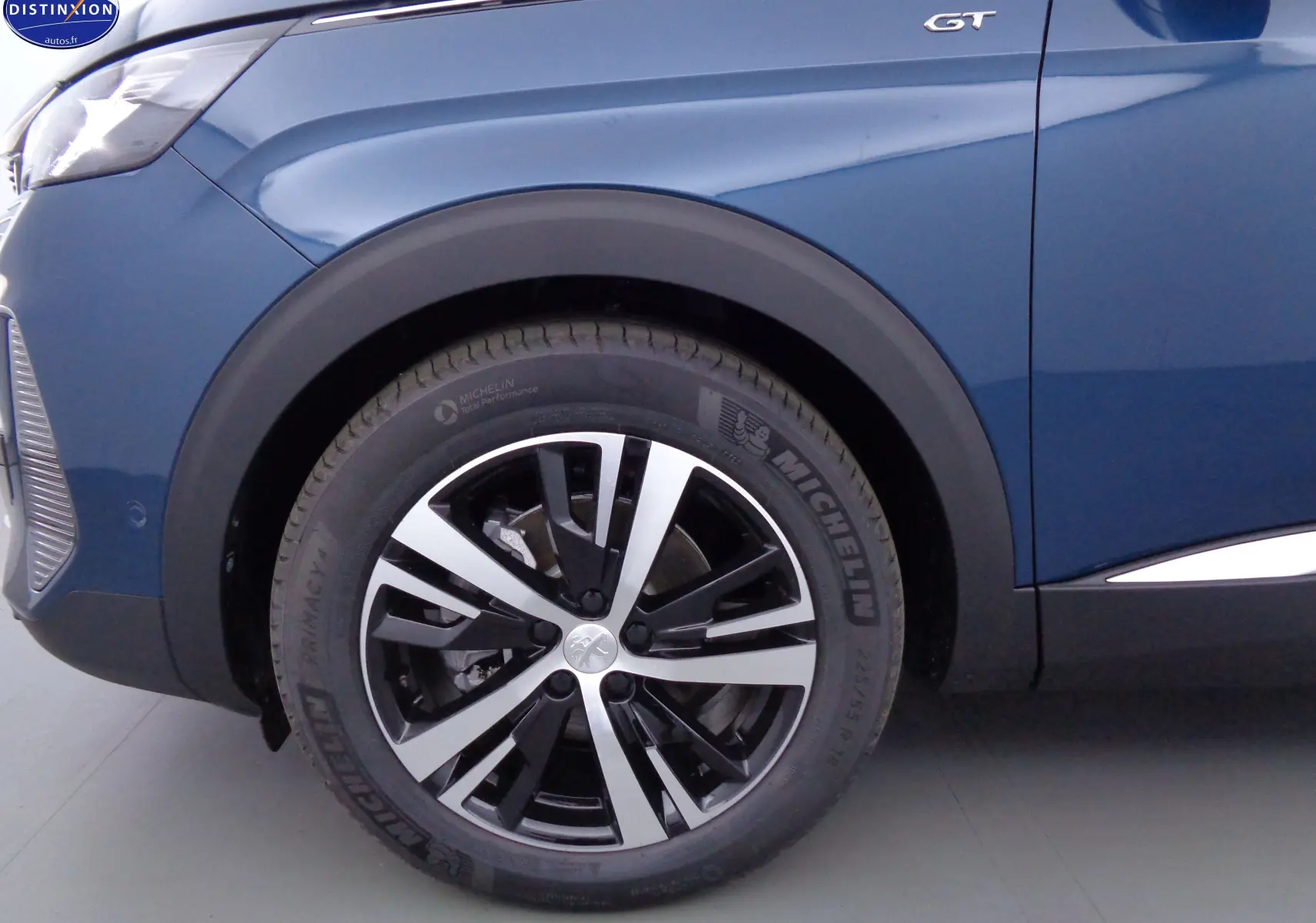 Gros plan sur la roue avant gauche et la portière bleu Célèbes métal du Peugeot 3008 GT avec logo GT visible.