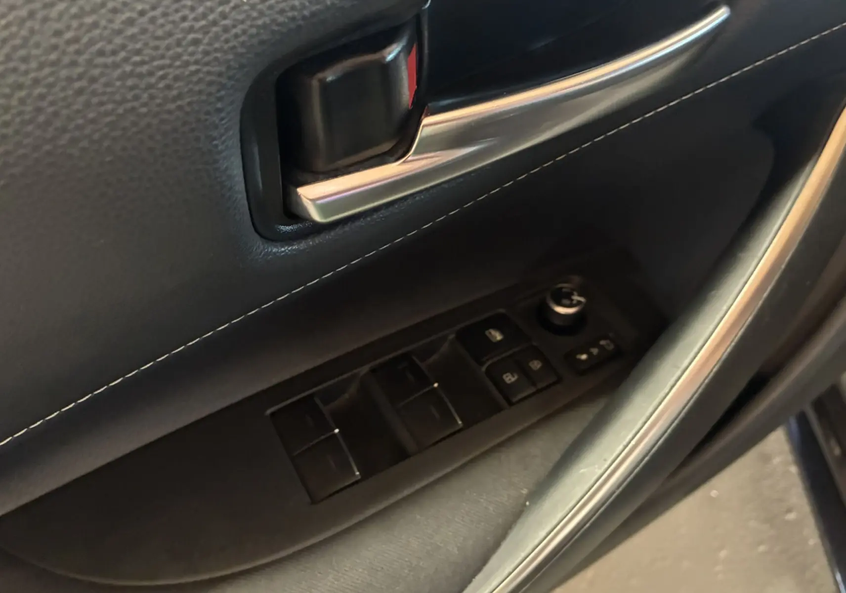 Gros plan sur la commande des vitres et rétroviseurs côté conducteur de la Toyota Corolla noire 2020, intérieur tissu noir.