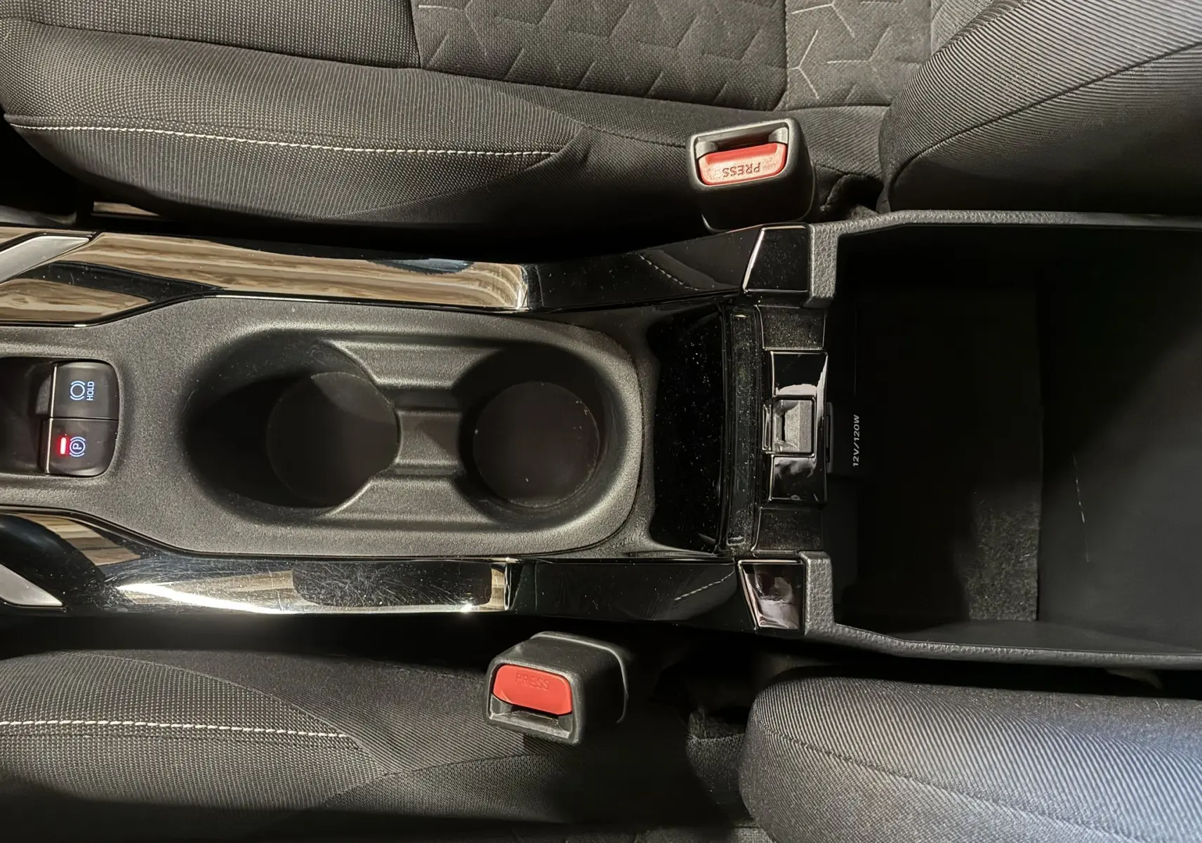 Vue plongeante sur la console centrale noire de la Toyota Corolla 1.8 122 DYNAMIC 2020 avec frein de parking automatique et porte-gobelets.