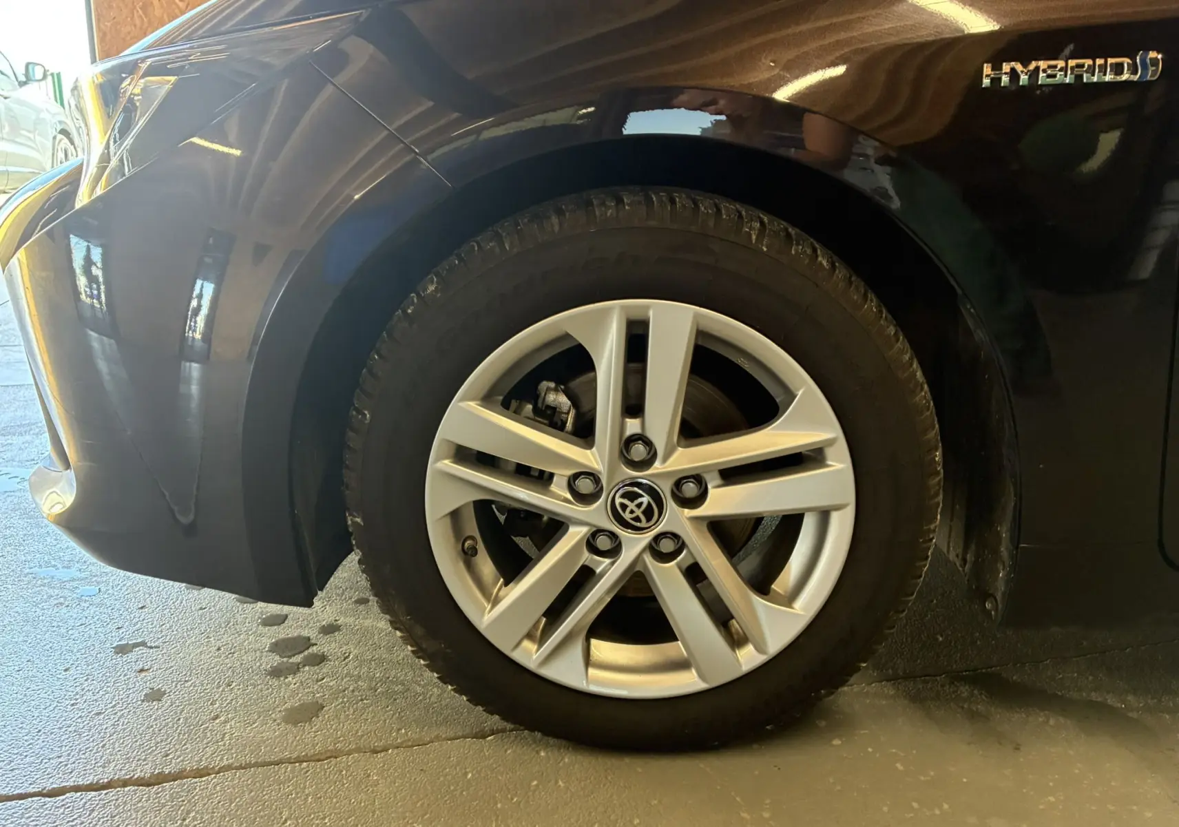 Gros plan sur la roue avant gauche de la Toyota Corolla noire 1.8 122 Dynamic avec jante alu et badge Hybrid visible.