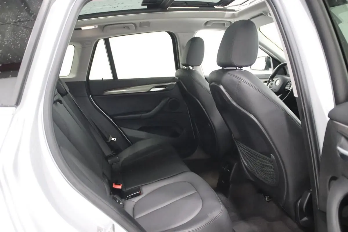 Vue intérieure côté gauche arrière du BMW X1 argenté, mettant en valeur les sièges en cuir noir et le toit ouvrant.