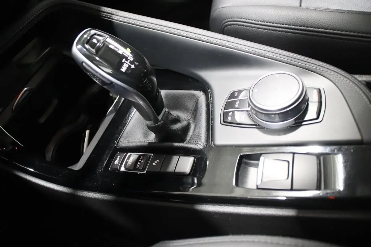 Gros plan sur la console centrale noire du BMW X1 sDRIVE 18D avec levier de vitesse automatique et commandes multimédia.