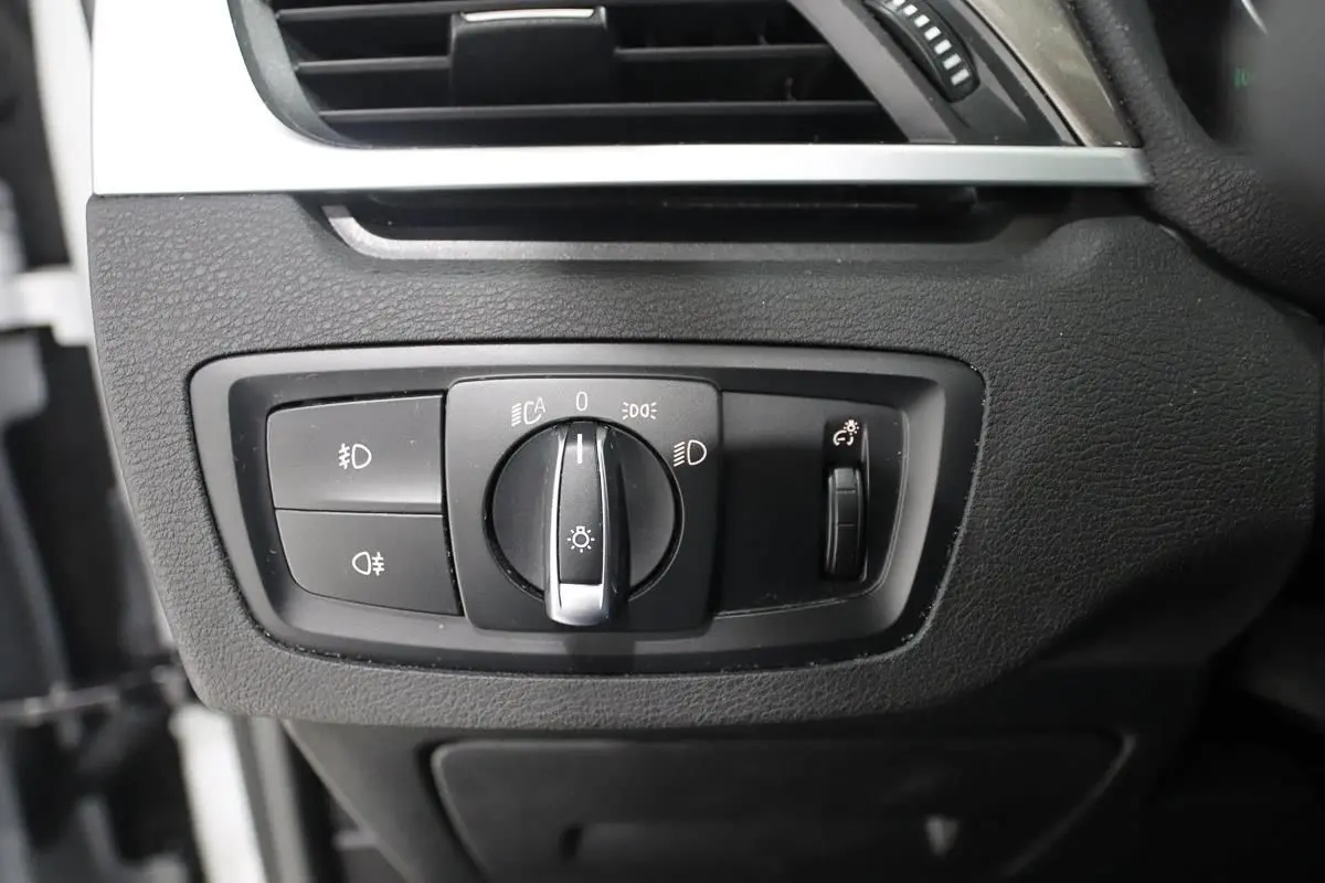 Gros plan sur le panneau de commande des phares du BMW X1 sDrive 18D, intérieur noir texturé.