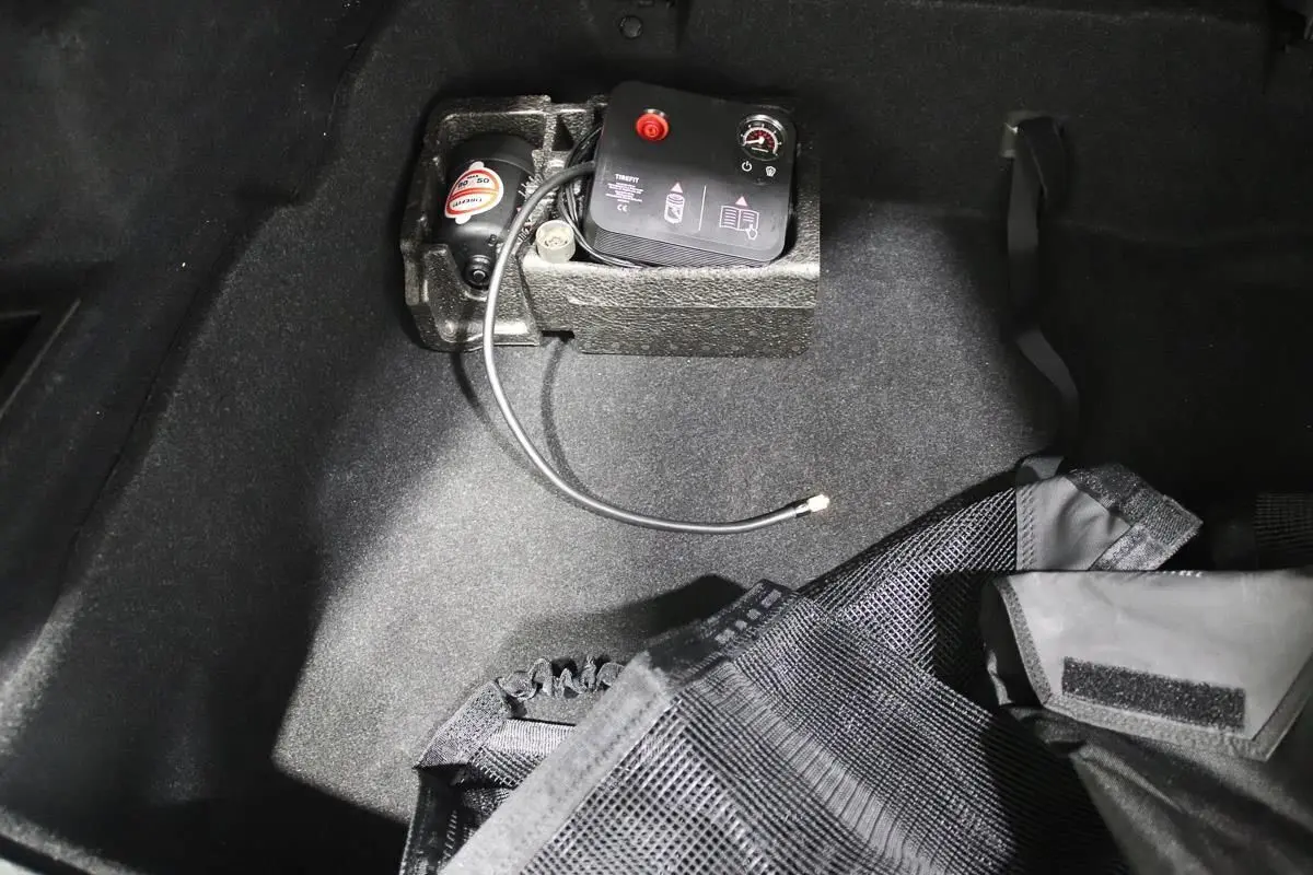 Gros plan sur le coffre d’un BMW X1 argenté, montrant un compresseur d’air intégré et un filet de rangement noir.