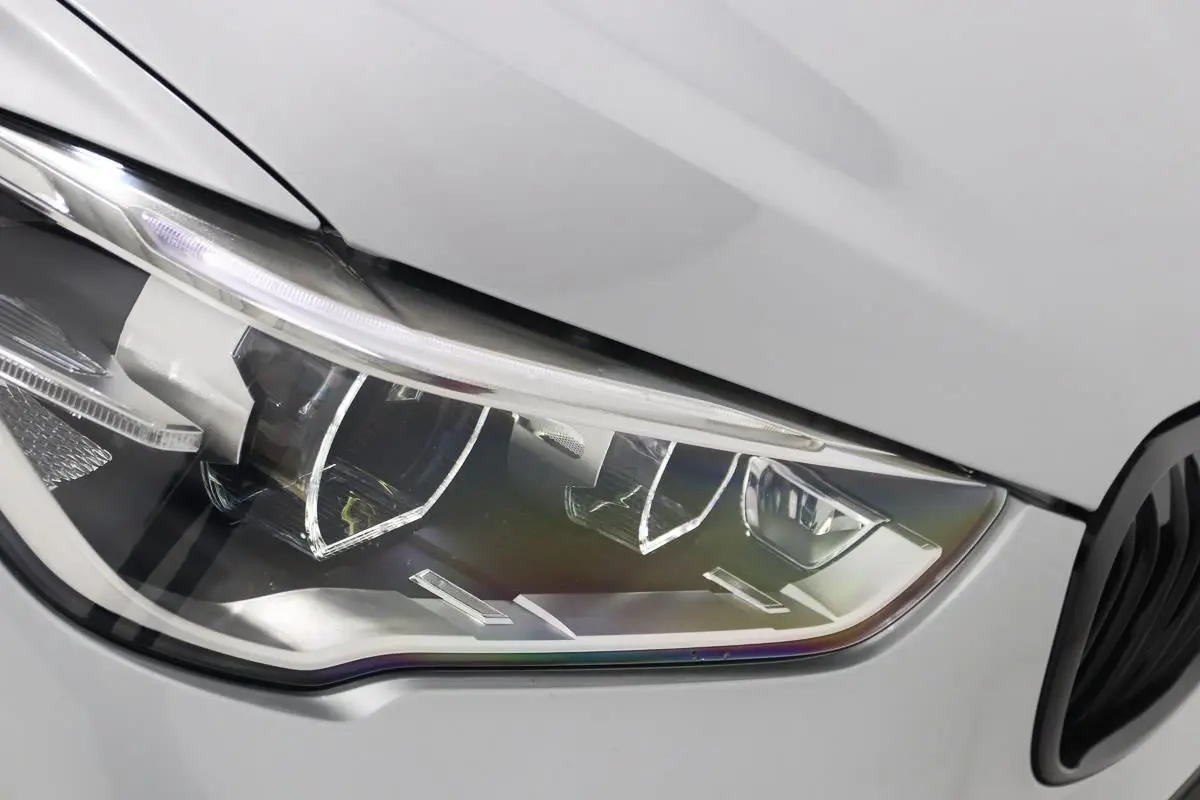 Gros plan sur le phare avant droit d’un BMW X1 sDrive 18D argent métallisé avec détails LED et calandre noire partielle visible.