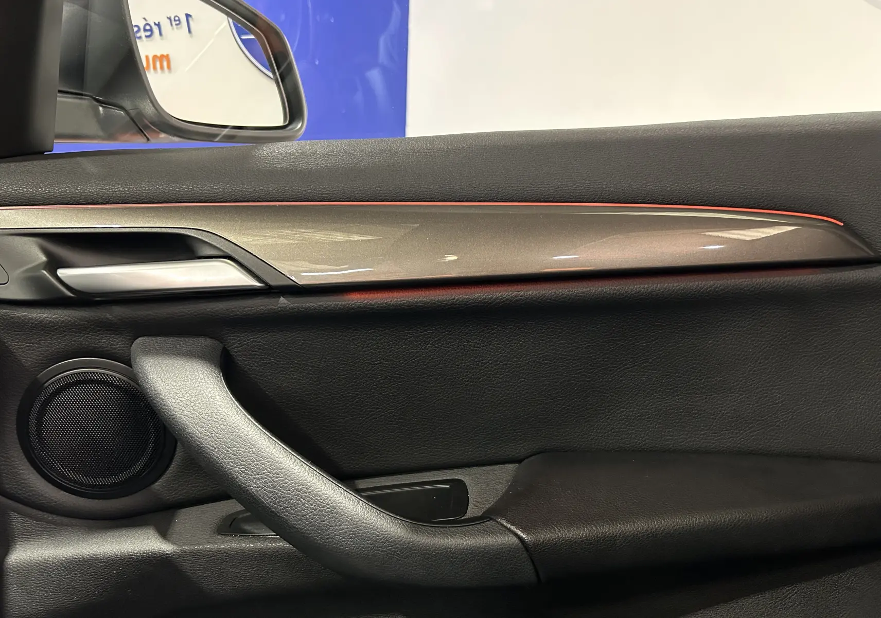 Détail de la porte intérieure côté conducteur d’un BMW X1 argent métallique, avec bande décorative et haut-parleur intégré.
