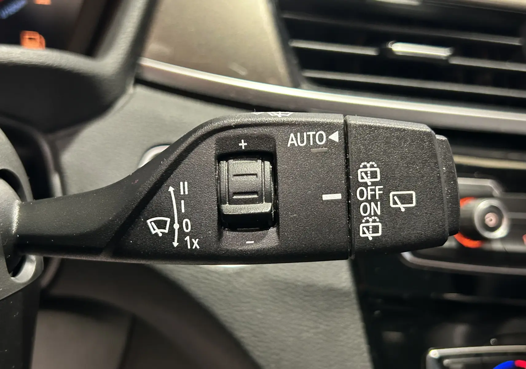 Gros plan sur la commande de l’essuie-glace intérieur du BMW X1 sDrive 18D 2019, avec tableau de bord en arrière-plan.