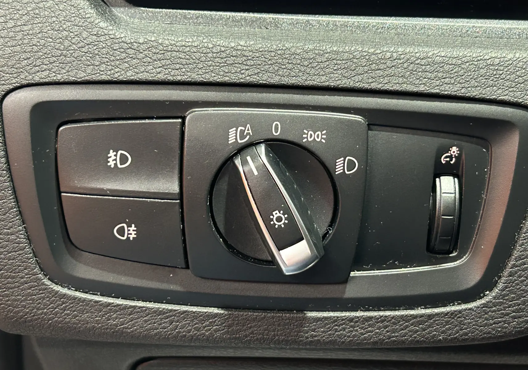 Gros plan sur le bouton de commande des phares et réglage de l'intensité lumineuse dans une BMW X1 argent métallisé de 2019.