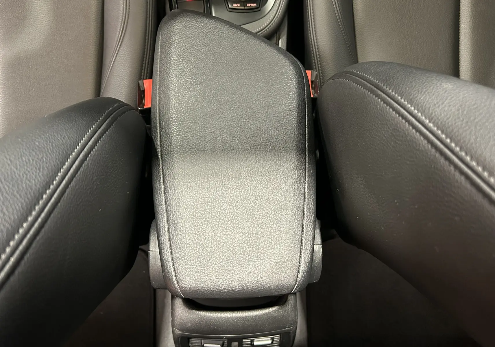 Vue rapprochée du couvercle de la console centrale en cuir noir entre les sièges avant d’un BMW X1 argent métallisé.