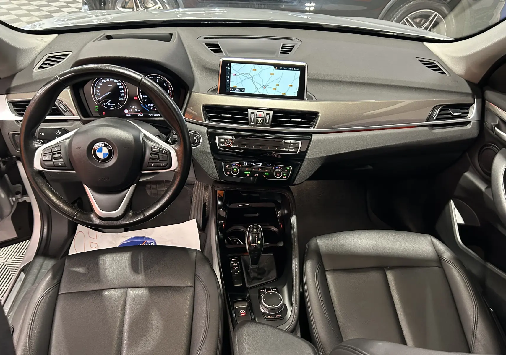 Vue intérieure avant du BMW X1 2019 montrant le tableau de bord, volant cuir multifonction et écran GPS central.