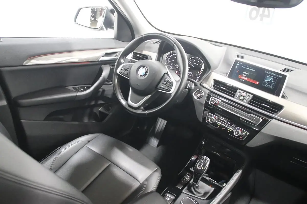 Vue intérieure côté conducteur du BMW X1 sDRIVE 18D 2019 avec tableau de bord moderne et sellerie cuir noire.
