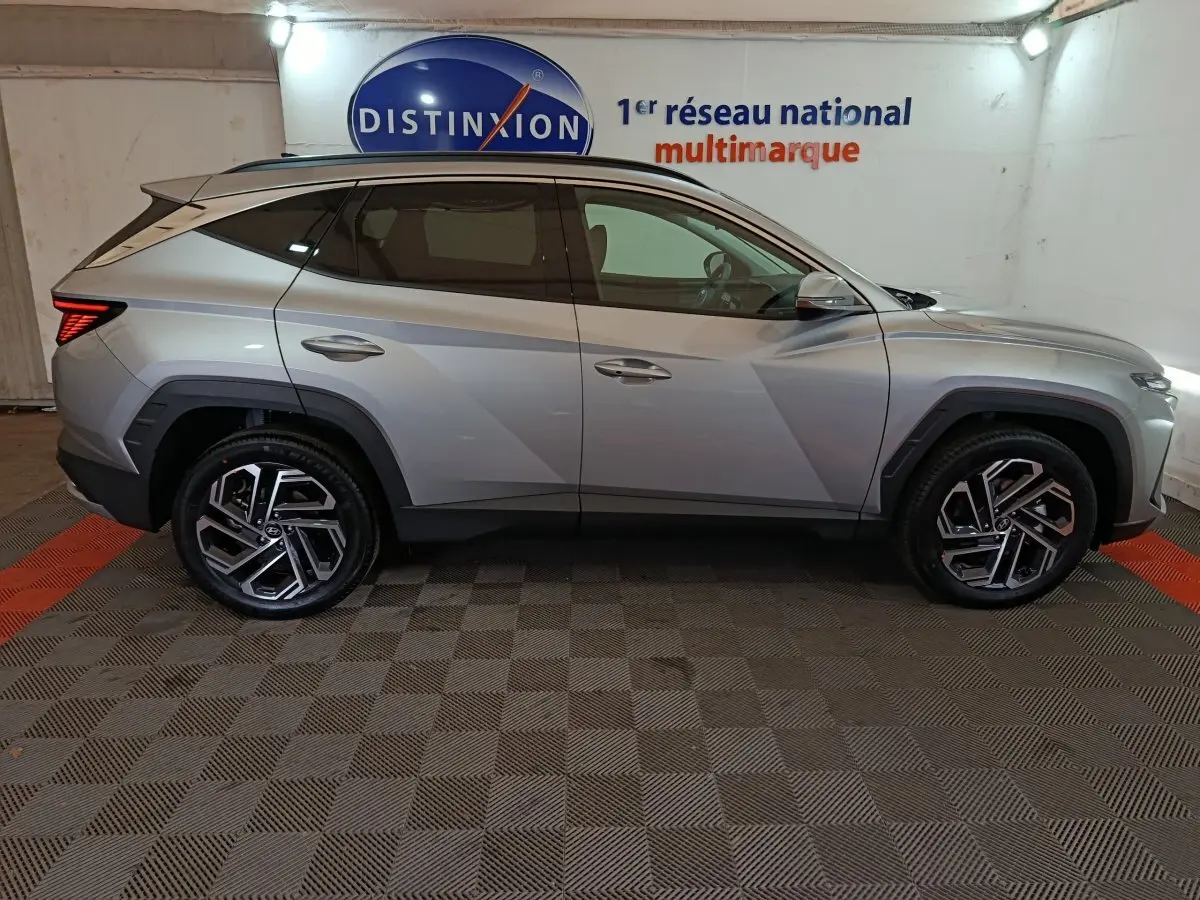 Vue latérale droite du Hyundai Tucson 1.6 Hybrid gris clair 2025, avec jantes alliage et toit noir contrasté.