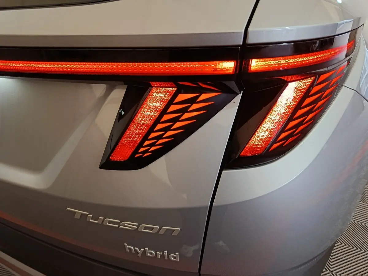 Gros plan sur le feu arrière droit rouge allumé d’un Hyundai Tucson hybride gris clair avec logo et inscription hybrid visibles.