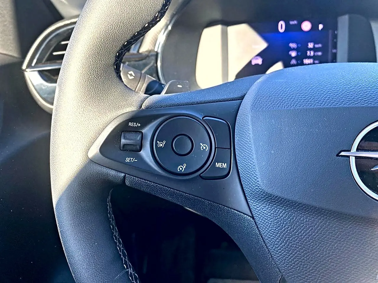 Gros plan sur le côté gauche du volant noir de l'Opel Corsa 2025 avec commandes de régulateur de vitesse et tableau de bord numérique.