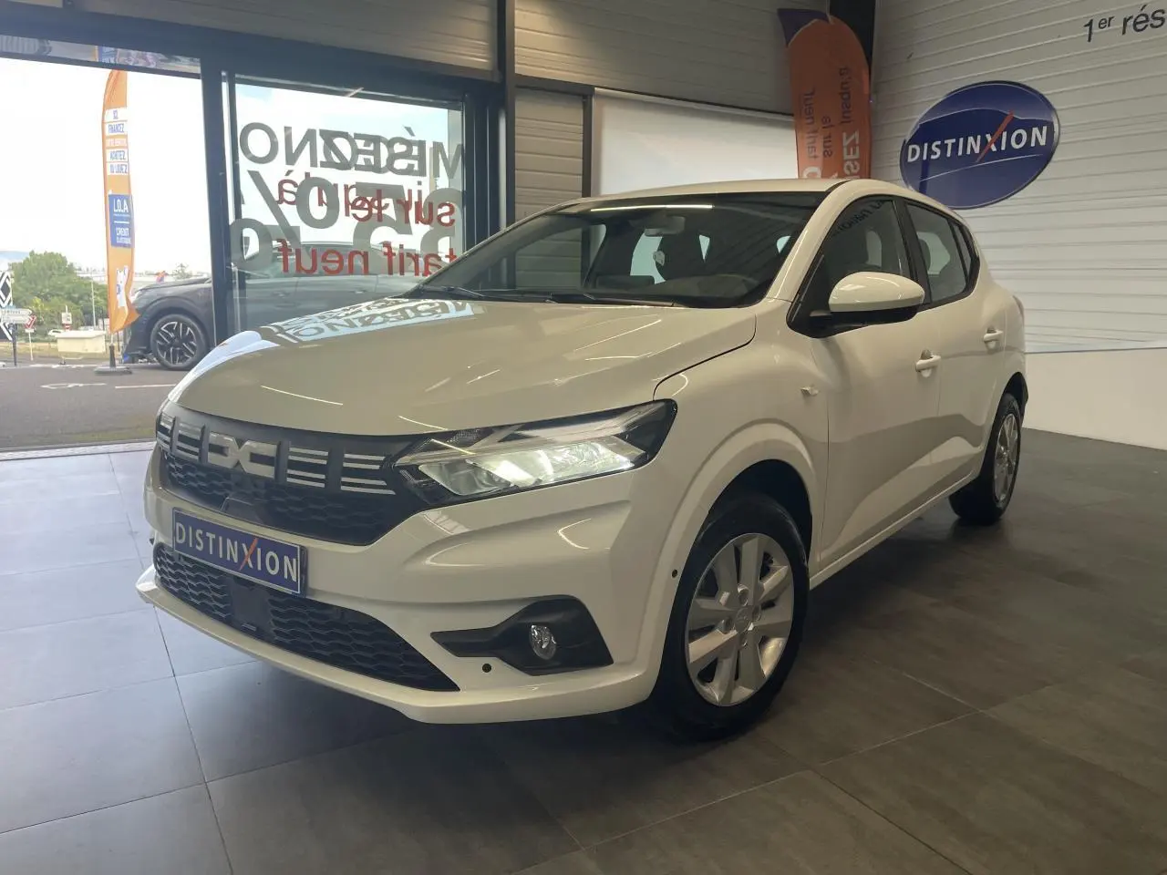 Dacia Sandero blanc vue 3/4 avant droit en showroom avec calandre noire et feux LED allumés.