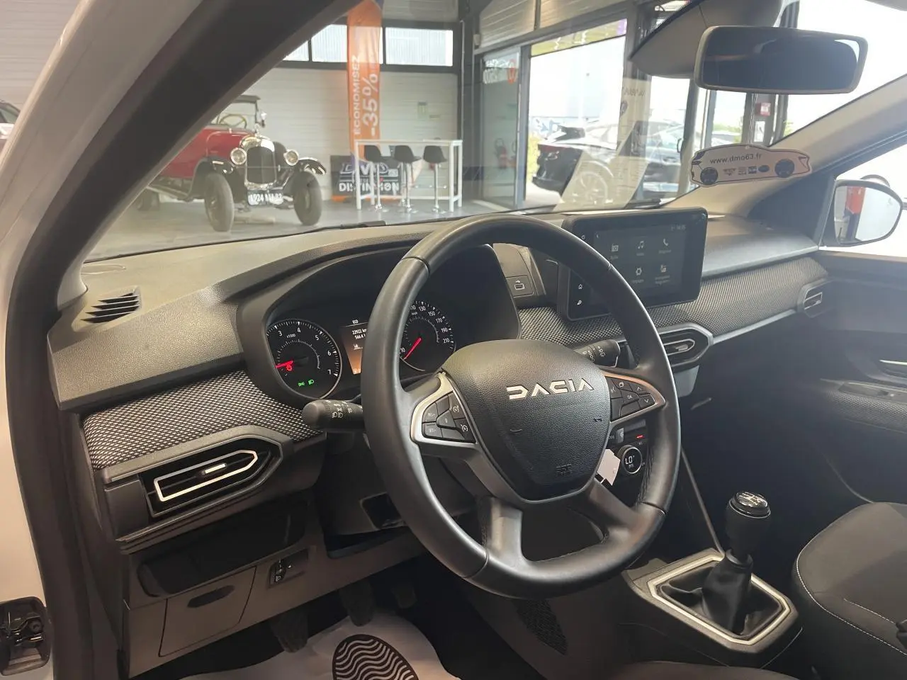 Vue intérieure côté conducteur de la Dacia Sandero blanche 2024, volant multifonction et tableau de bord moderne.
