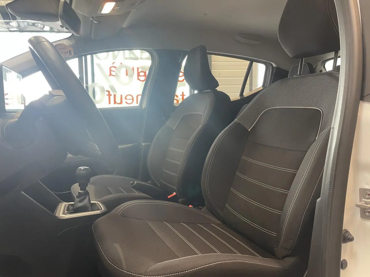 Vue intérieure côté gauche montrant les sièges avant noirs et la boîte manuelle d'une Dacia Sandero blanche 2024.