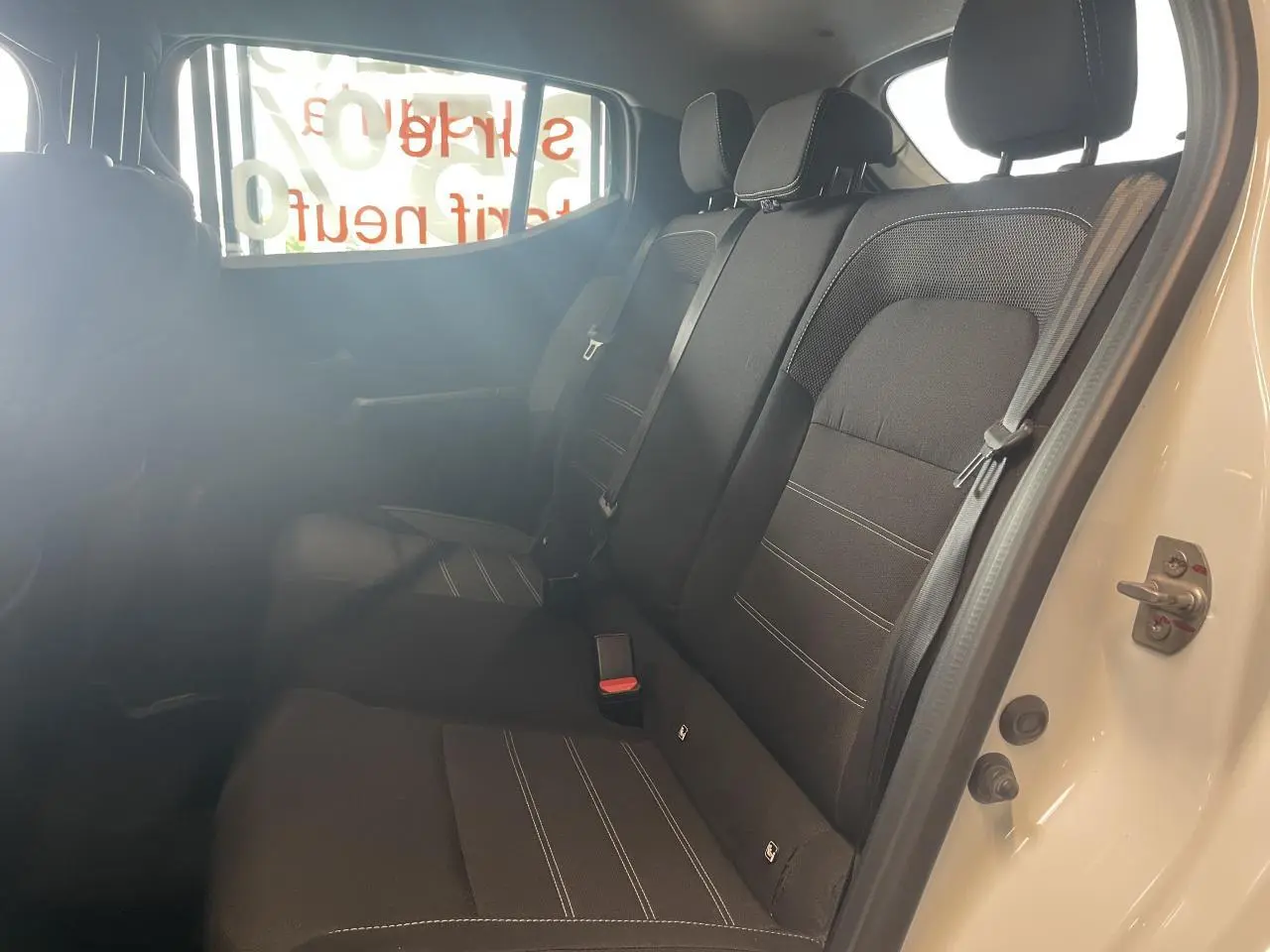 Vue intérieure côté droit sur la banquette arrière noire de la Dacia Sandero blanche 2024 avec ceintures de sécurité visibles.
