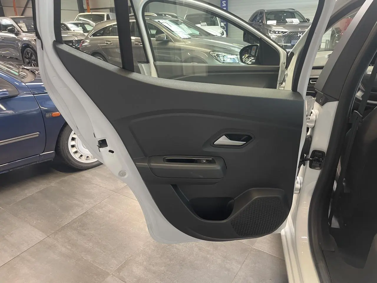 Vue intérieure de la porte arrière gauche blanche d'une Dacia Sandero 2024 avec habillage noir et poignée argentée.