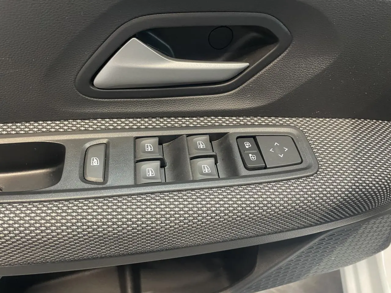 Détail de la porte avant gauche de la Dacia Sandero 2024, avec commandes électriques et revêtement tissu gris.
