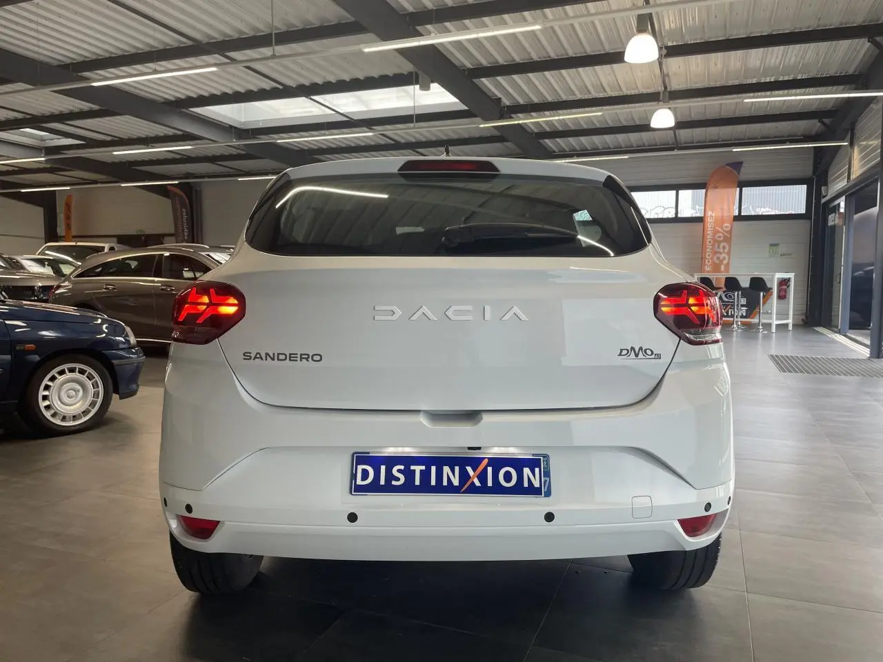 Vue arrière d'une Dacia Sandero blanche 2024 avec feux LED allumés dans un showroom.