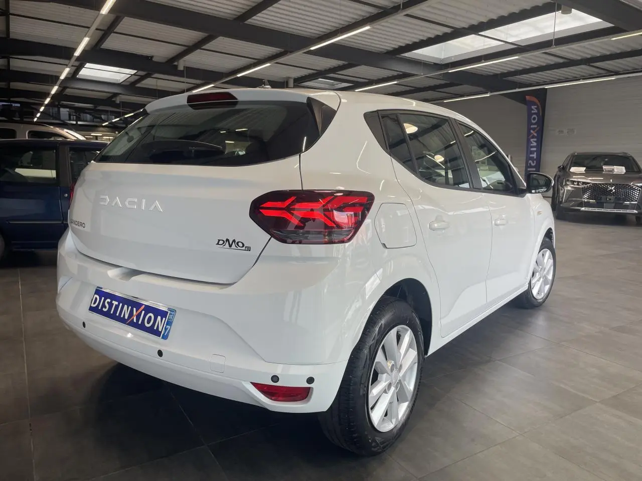Vue 3/4 arrière droite d'une Dacia Sandero blanche 2024 avec feux LED et enjoliveurs Sorane en showroom.