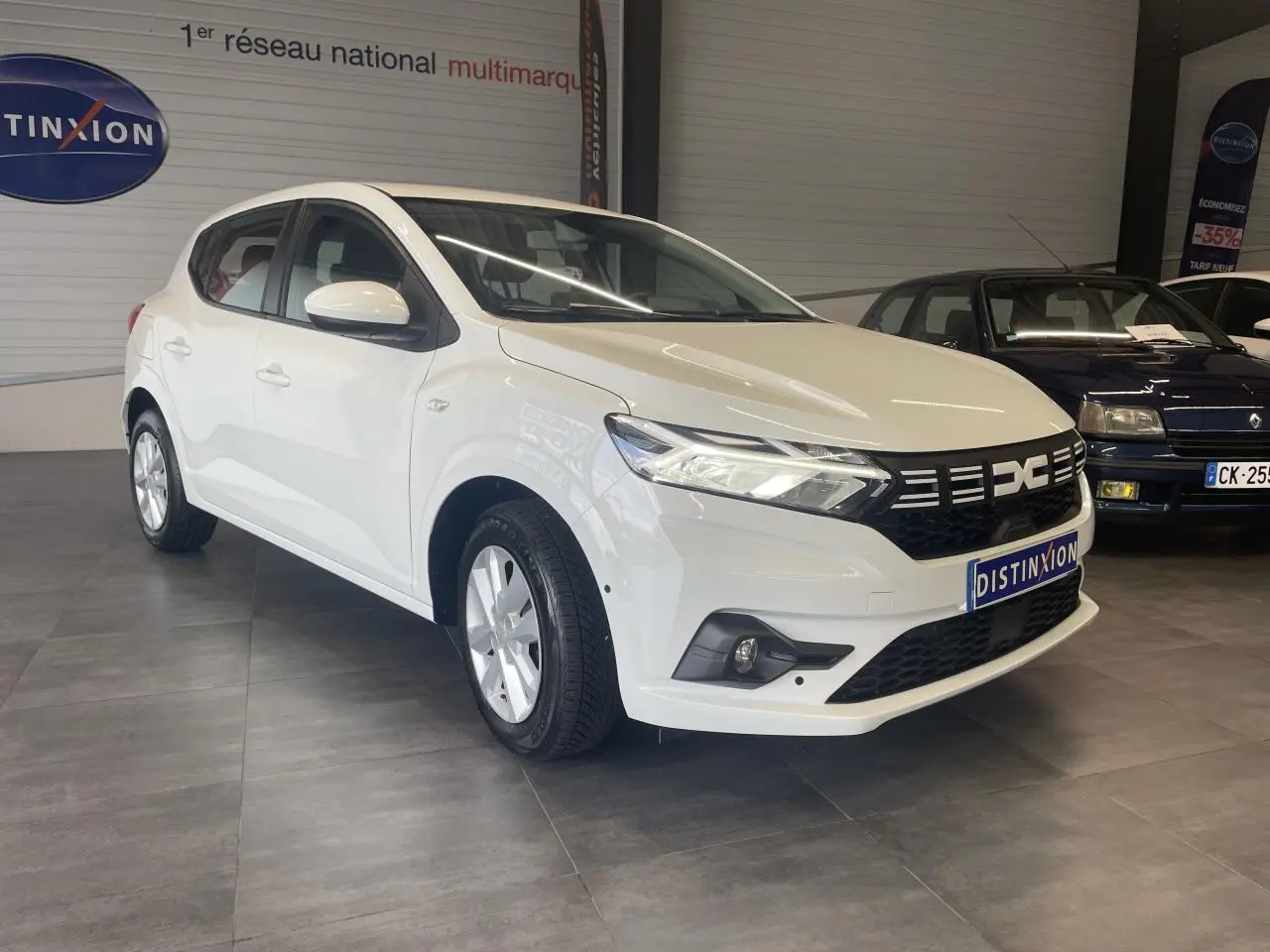 Vue 3/4 avant d'une Dacia Sandero blanche 2024 avec calandre noire et jantes à enjoliveurs.