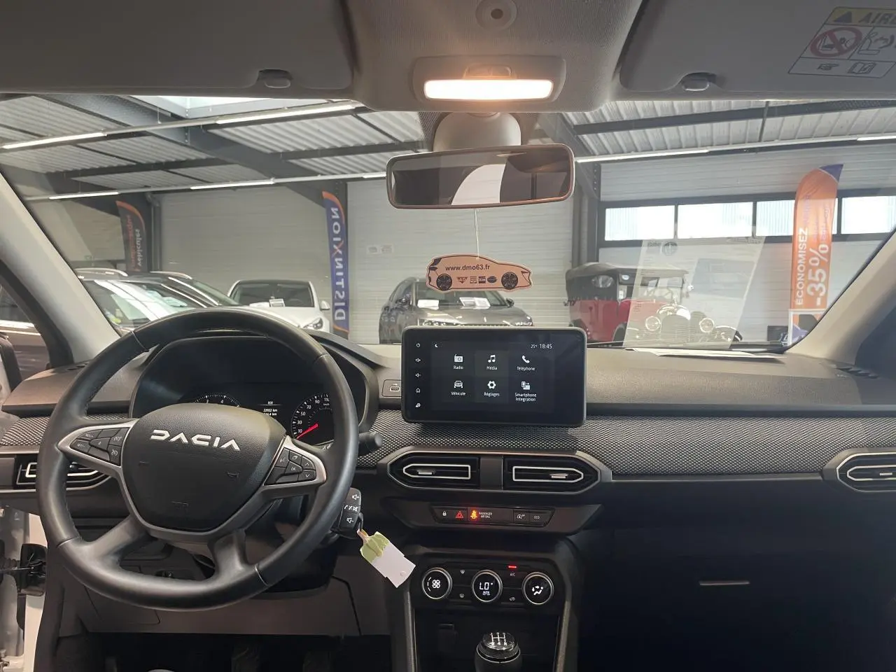Vue intérieure avant du tableau de bord noir et volant DACIA d'une Sandero blanche avec écran tactile central allumé.