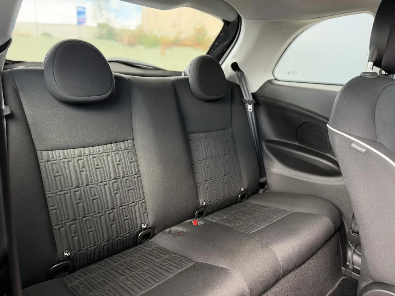 Vue intérieure arrière de la Fiat 500 électrique 2024, montrant la banquette noire avec motifs FIAT embossés.